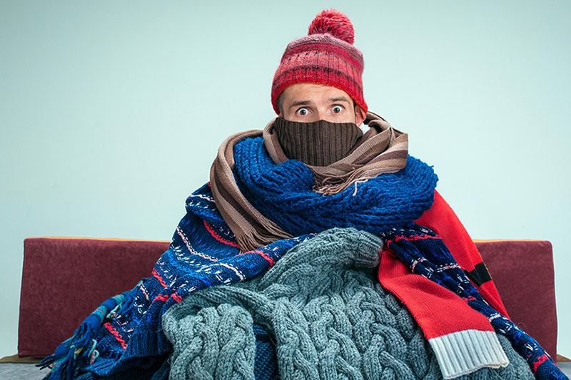 10 Things to Consider When Buying a New Furnace. A person under a bunch of blankets because their furnace broke.